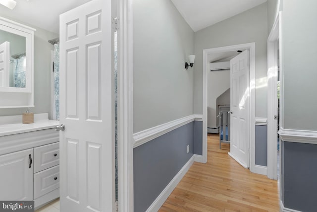 hall featuring a wall unit AC, light wood finished floors, baseboard heating, and baseboards