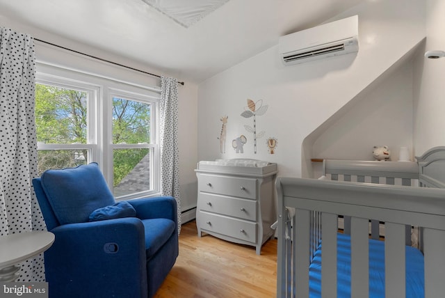 bedroom with a wall mounted air conditioner, a crib, baseboard heating, and light wood-type flooring