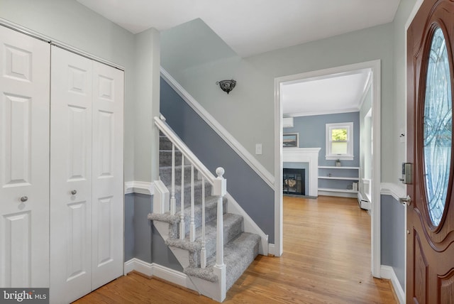 staircase with ornamental molding, a fireplace with flush hearth, wood finished floors, and baseboards