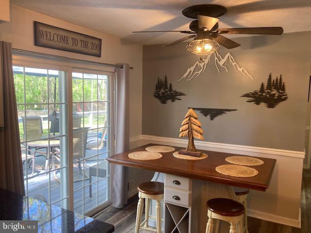 dining space featuring dark wood-style flooring, a ceiling fan, and a wainscoted wall
