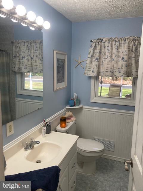 bathroom with visible vents, vanity, toilet, a textured ceiling, and tile patterned floors