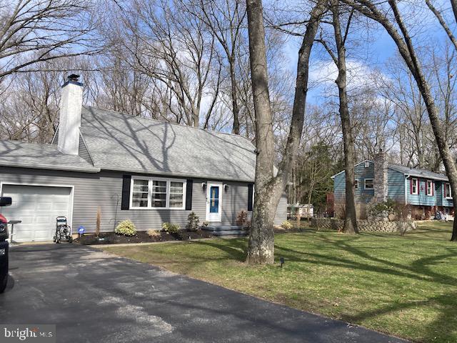 ranch-style house featuring an attached garage, a chimney, driveway, and a front yard
