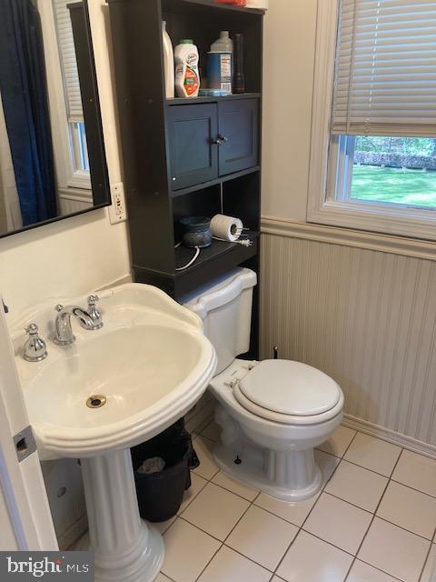 half bath with tile patterned flooring, a wainscoted wall, and toilet