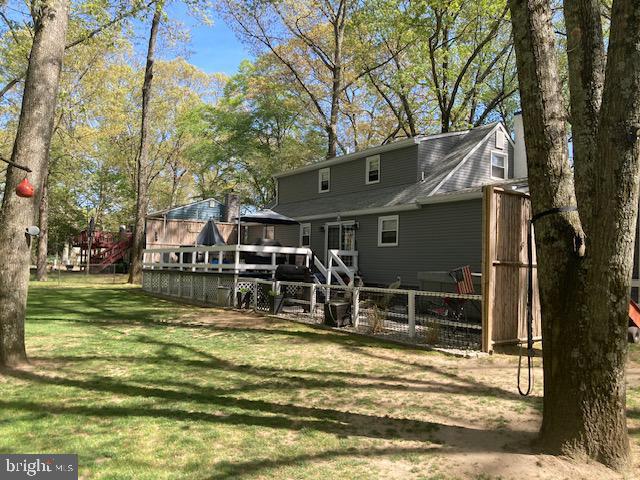 back of property with fence, a wooden deck, and a yard