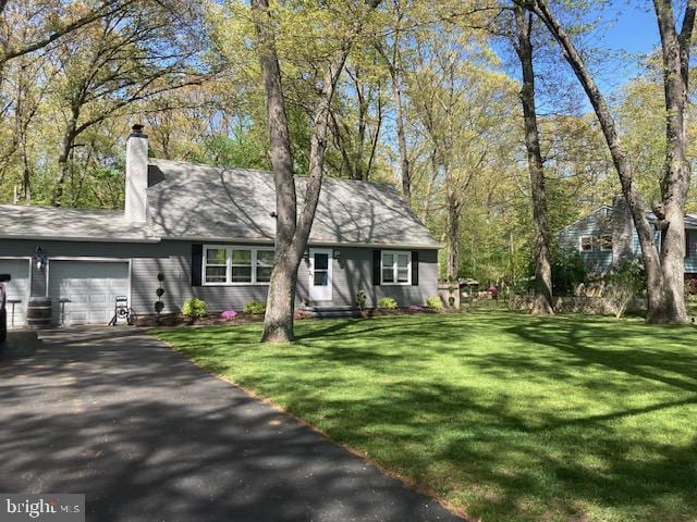 ranch-style house with an attached garage, a chimney, a front lawn, and aphalt driveway