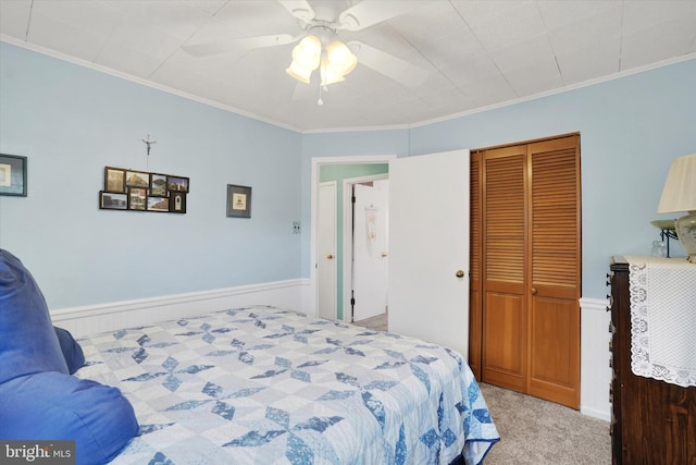 bedroom with a closet, crown molding, wainscoting, light carpet, and a ceiling fan