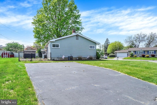 view of side of property with fence, a chimney, central air condition unit, a yard, and driveway