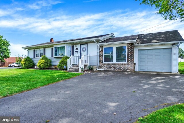 ranch-style home featuring a garage, aphalt driveway, a front yard, a chimney, and brick siding