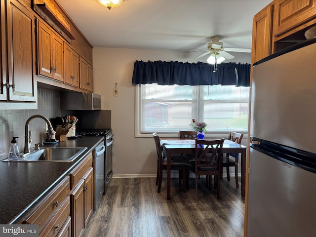 kitchen with a sink, dark countertops, brown cabinets, a ceiling fan, and appliances with stainless steel finishes