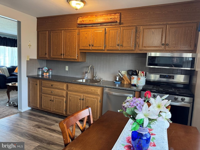 kitchen with appliances with stainless steel finishes, dark countertops, brown cabinets, a sink, and dark wood-type flooring