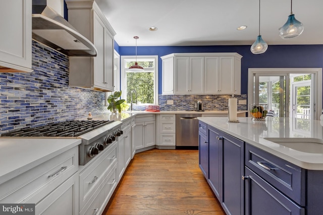 kitchen with wall chimney range hood, backsplash, appliances with stainless steel finishes, and white cabinetry