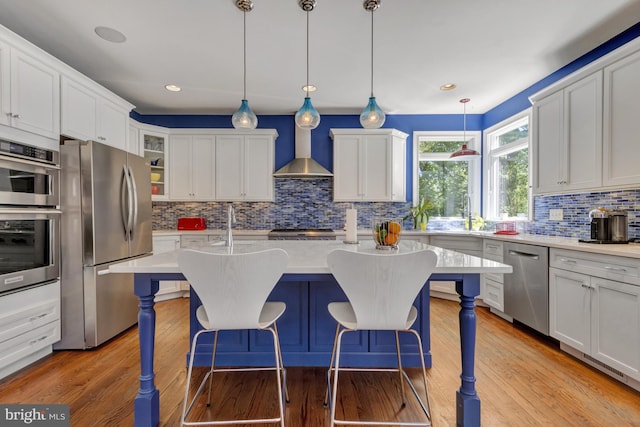 kitchen featuring light countertops, decorative backsplash, appliances with stainless steel finishes, and wall chimney range hood
