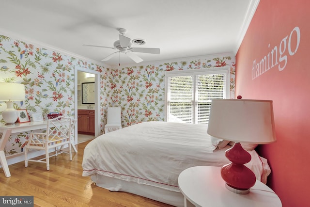 bedroom featuring ceiling fan, crown molding, light wood-type flooring, ensuite bathroom, and wallpapered walls