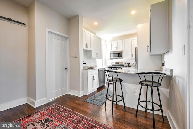 kitchen with a peninsula, a breakfast bar, dark wood-type flooring, light stone counters, and appliances with stainless steel finishes
