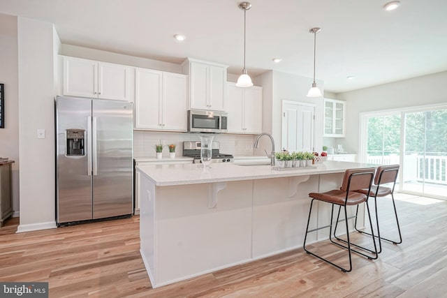 kitchen featuring white cabinets, stainless steel appliances, decorative backsplash, and light wood-style flooring