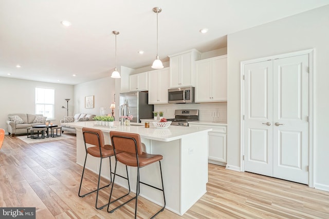 kitchen with light wood finished floors, an island with sink, a kitchen bar, and stainless steel appliances