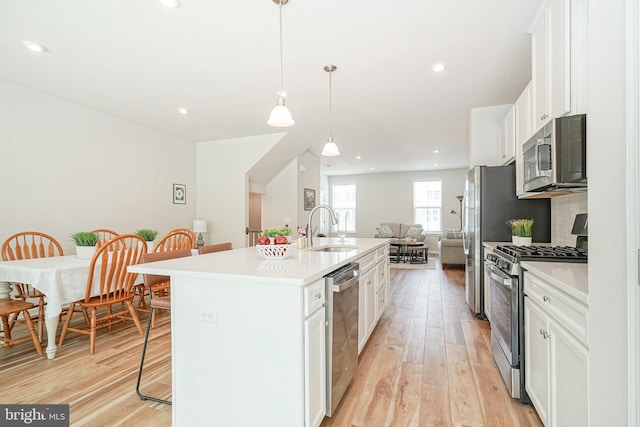 kitchen featuring a sink, open floor plan, a breakfast bar, stainless steel appliances, and light wood-style flooring