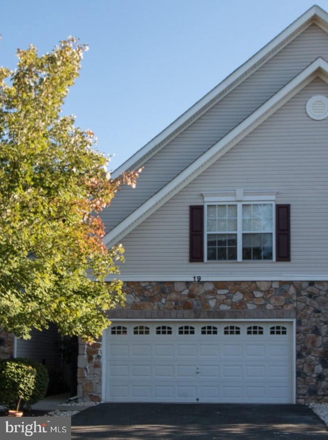 view of side of property featuring driveway, stone siding, and an attached garage