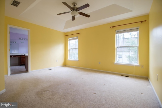 unfurnished room with a raised ceiling, visible vents, light colored carpet, and a ceiling fan