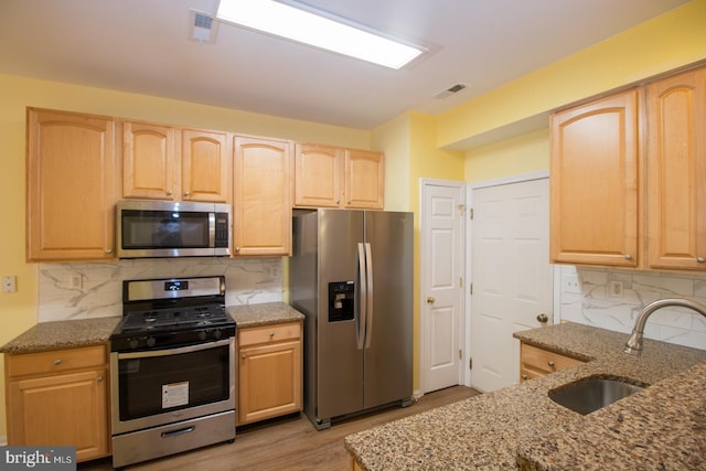 kitchen with a sink, stone counters, light brown cabinetry, visible vents, and appliances with stainless steel finishes