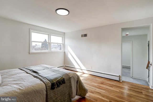 bedroom featuring wood finished floors, a baseboard radiator, a baseboard heating unit, baseboards, and visible vents