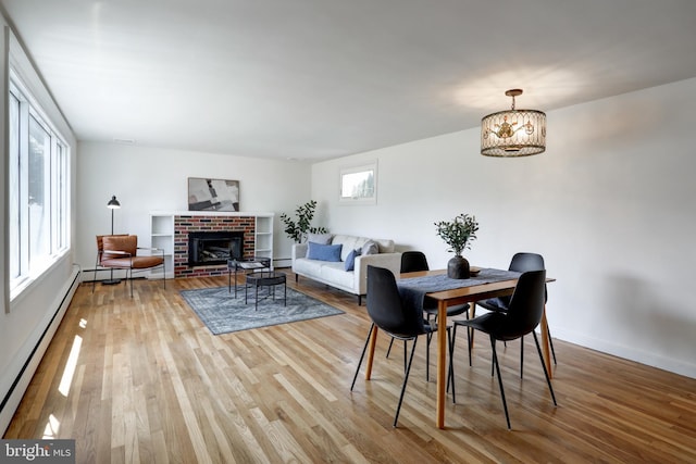dining space with a brick fireplace, wood finished floors, baseboard heating, and baseboards