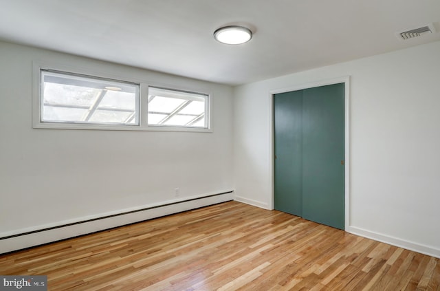 unfurnished bedroom featuring a baseboard heating unit, light wood-style floors, a closet, visible vents, and baseboards