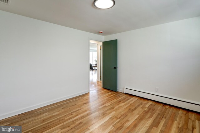unfurnished room with light wood-style floors, visible vents, a baseboard heating unit, and baseboards