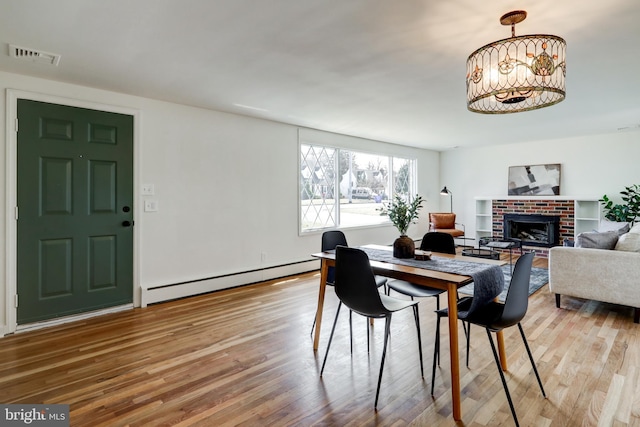 dining area featuring a chandelier, a fireplace, visible vents, wood finished floors, and a baseboard radiator