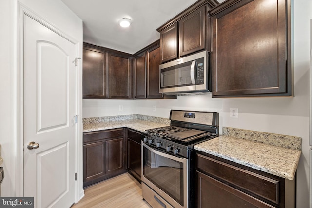 kitchen with appliances with stainless steel finishes, dark brown cabinetry, light wood-style flooring, and light stone countertops