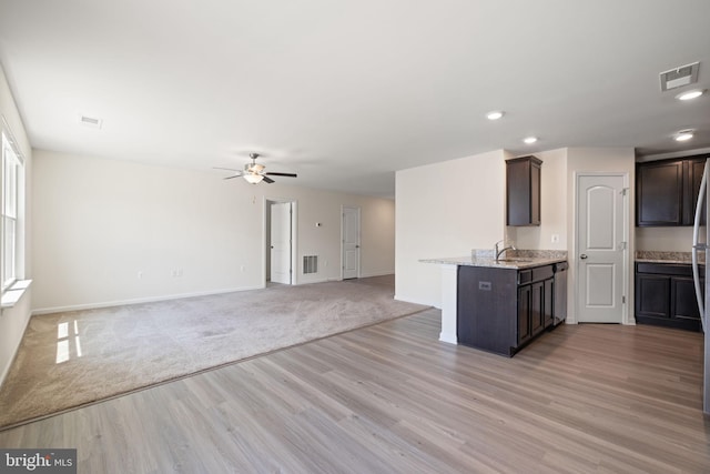 kitchen featuring visible vents, dark brown cabinetry, ceiling fan, a sink, and light wood-style flooring