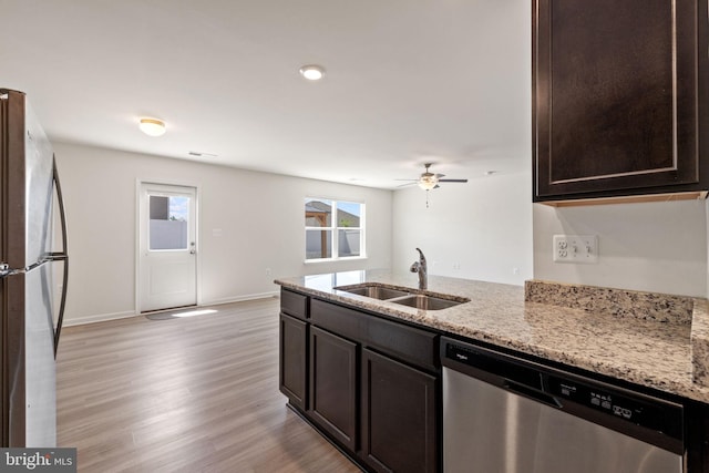 kitchen with dark brown cabinetry, appliances with stainless steel finishes, a sink, and light stone counters