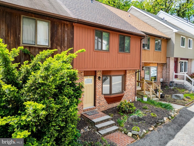 view of property featuring brick siding and roof with shingles