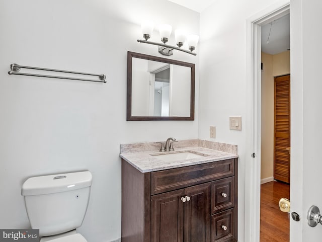 half bathroom featuring toilet, wood finished floors, and vanity