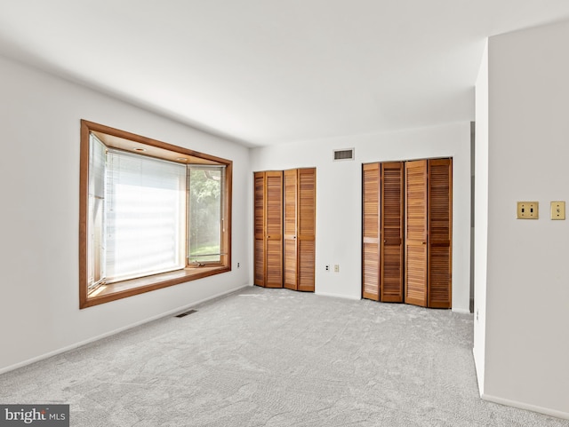 unfurnished bedroom featuring baseboards, carpet, two closets, and visible vents