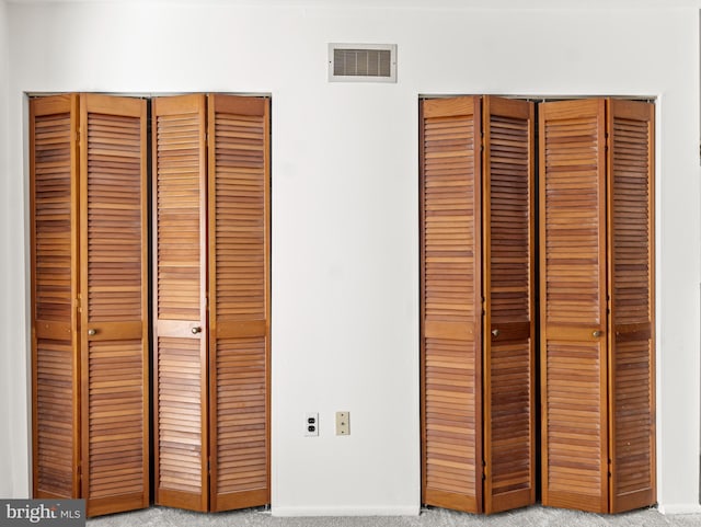 unfurnished bedroom with two closets, baseboards, visible vents, and carpet