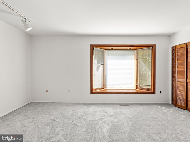 empty room featuring carpet flooring, baseboards, visible vents, and track lighting