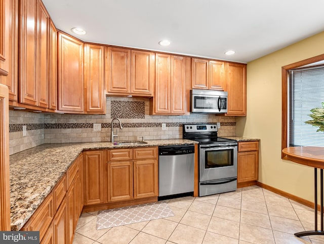 kitchen with light stone countertops, a sink, backsplash, light tile patterned floors, and stainless steel appliances