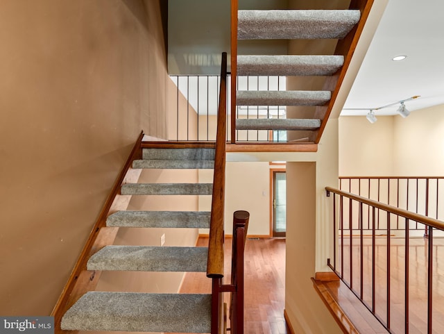 staircase with rail lighting and wood finished floors