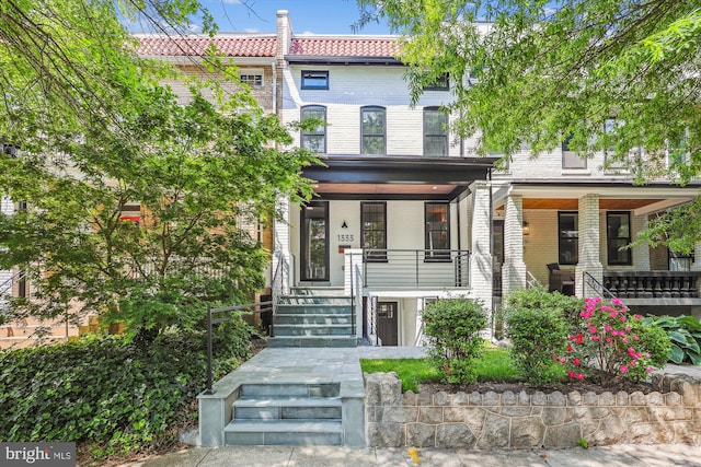 multi unit property featuring covered porch, a tiled roof, stairway, and brick siding