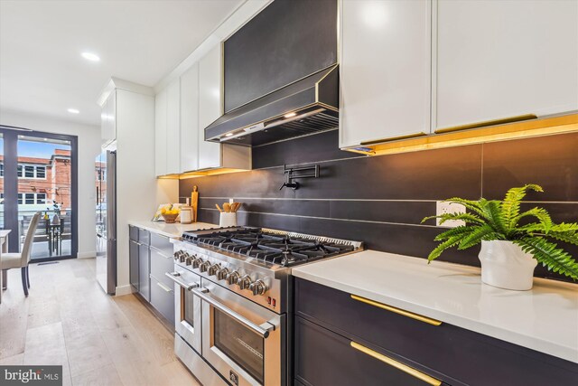kitchen featuring stainless steel appliances, wall chimney exhaust hood, tasteful backsplash, light countertops, and baseboards