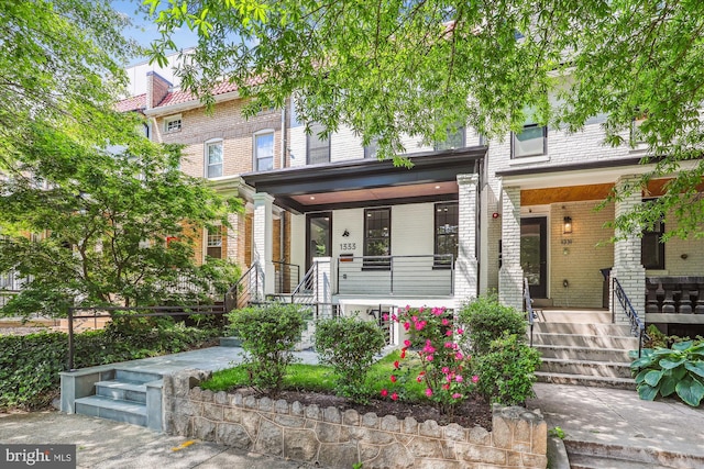 multi unit property with brick siding, a porch, and stairway