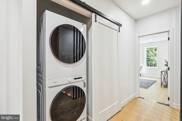 clothes washing area with stacked washer / dryer, light wood-style floors, a barn door, and recessed lighting