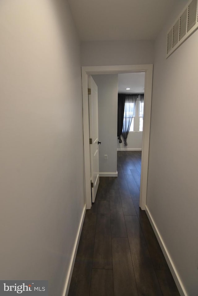hall featuring dark wood-type flooring, visible vents, and baseboards