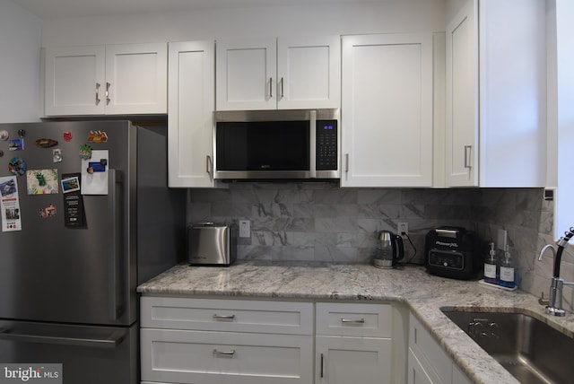 kitchen with light stone countertops, decorative backsplash, appliances with stainless steel finishes, a sink, and white cabinetry