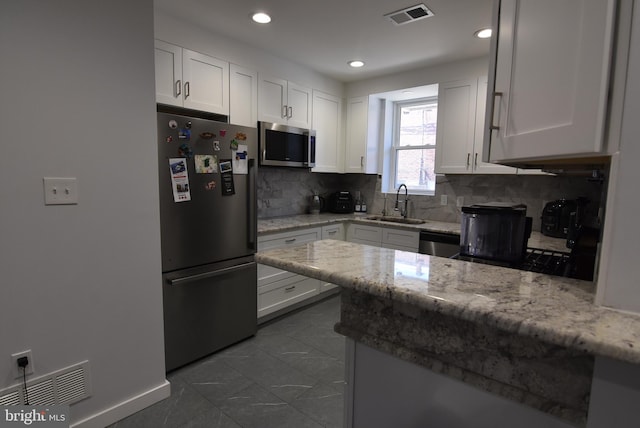 kitchen featuring stainless steel appliances, backsplash, a sink, white cabinetry, and visible vents