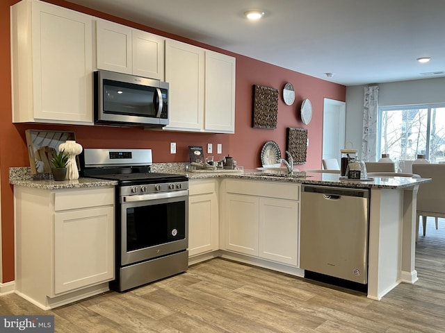 kitchen featuring white cabinetry, a peninsula, appliances with stainless steel finishes, and light wood-style floors