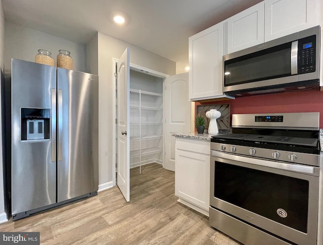 kitchen with light wood-type flooring, light stone counters, appliances with stainless steel finishes, and white cabinetry