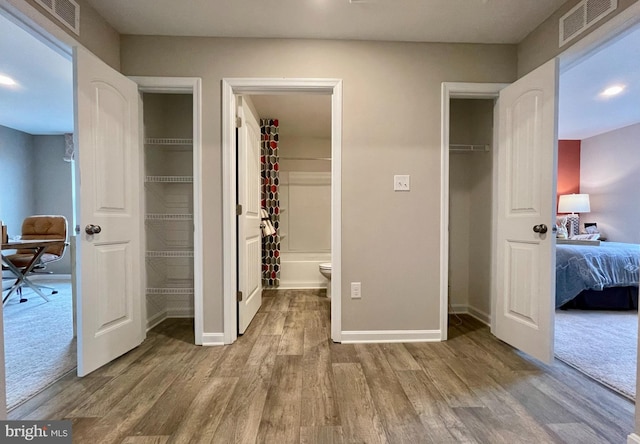 bedroom with baseboards, visible vents, wood finished floors, and a walk in closet