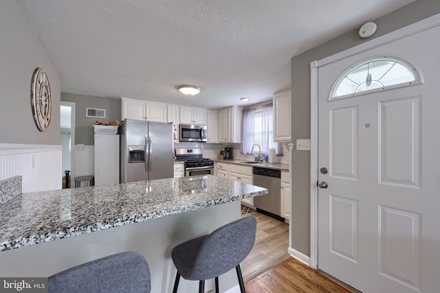 kitchen featuring light stone counters, appliances with stainless steel finishes, light wood-type flooring, a sink, and visible vents